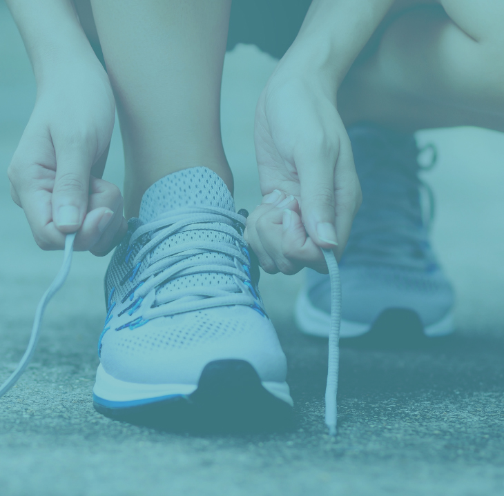 Person tying blue and white running shoe laces outdoors on pavement.
