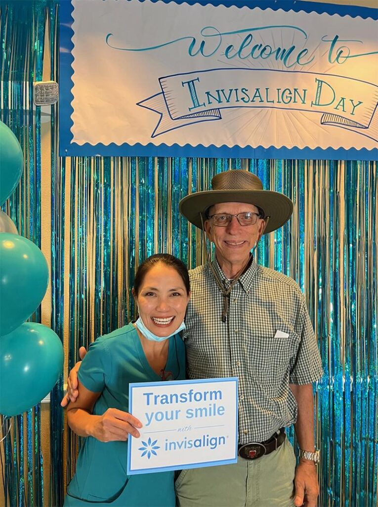 Two people posing at Invisalign Day event with "Transform Your Smile" sign and decorations.