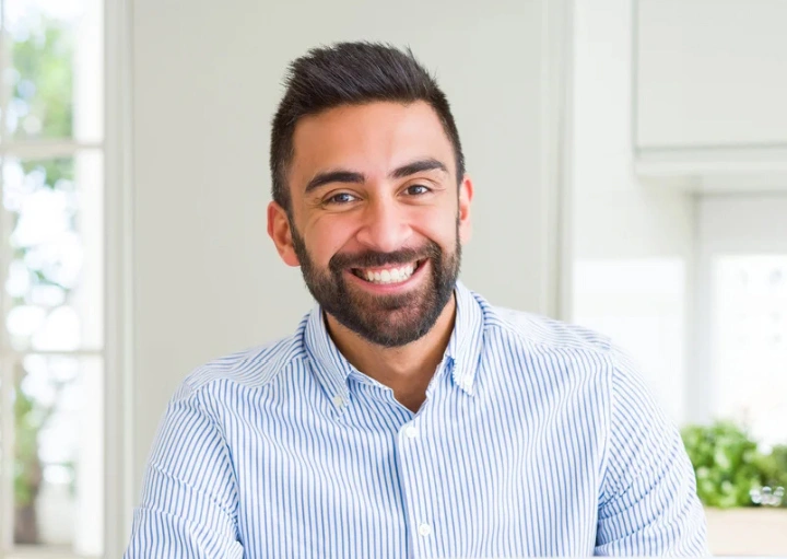 Smiling male dental professional in blue striped shirt, modern bright office setting.