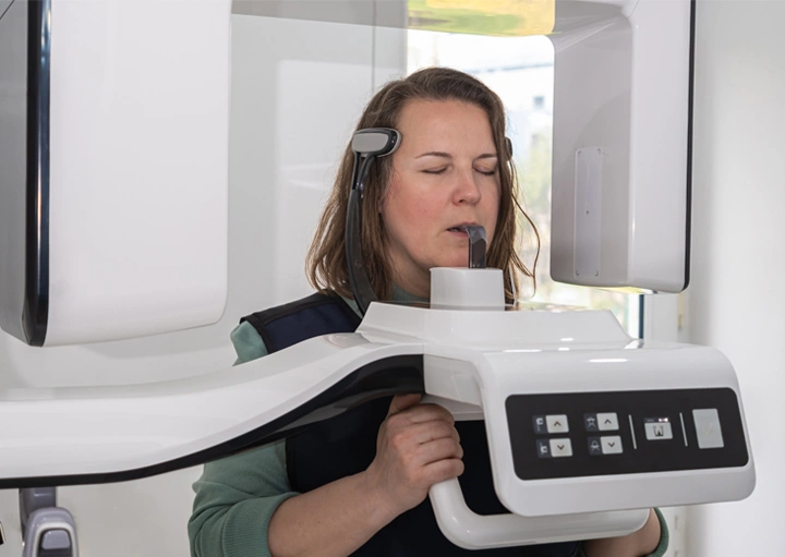 Dental professional operating panoramic X-ray machine on patient in modern dental office setting.