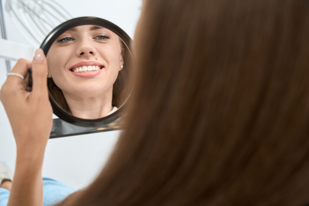 A woman gazes at her reflection in a mirror, examining her features with a thoughtful expression.
